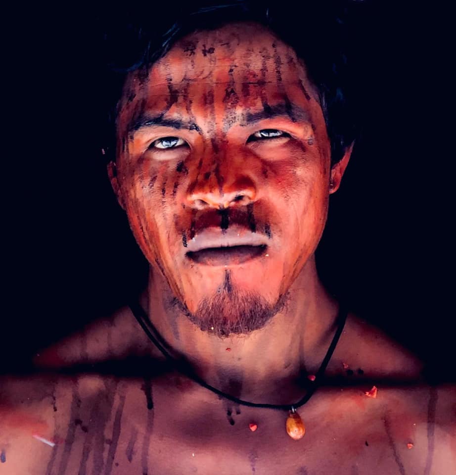 O líder indígena Guajajara Paulo Paulino Guajajara, que foi morto a tiros em uma suposta emboscada de madeireiros na Amazônia. Seguindo rituais tradicionais de proteção, seu rosto é pintado com tinta vermelha de sementes de urucum e tinta preta de jenipapo ralado. Imagem cortesia de Patrick Raynaud/Mídia Índia.